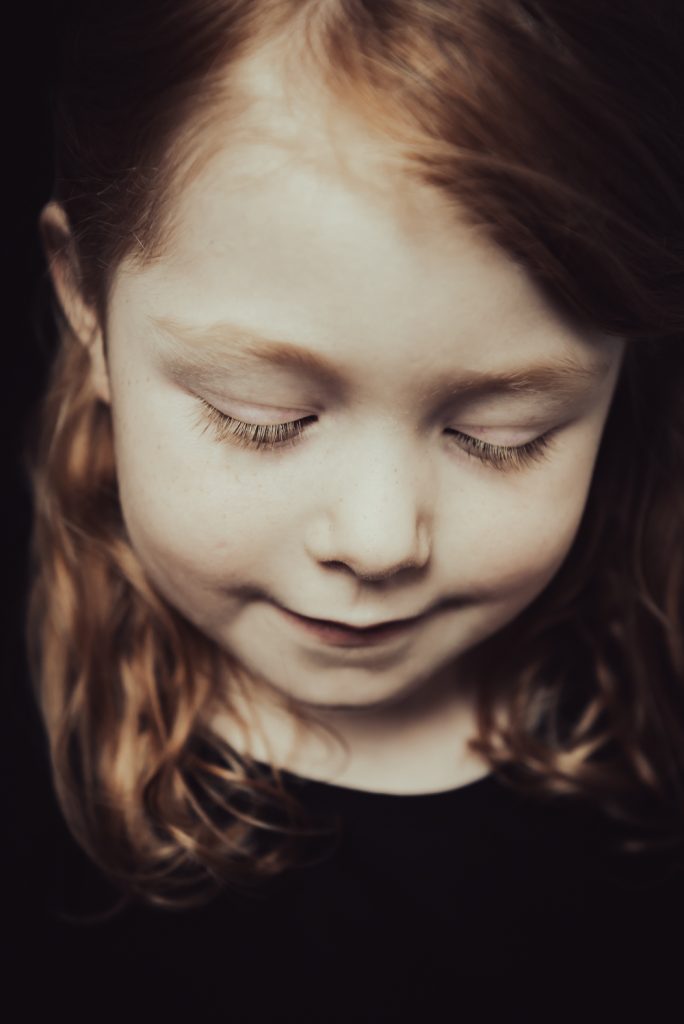 portretfoto van jong meisje met rood haar en sproetjes. ze kijkt sereen naar beneden alsof haar ogen dicht zijn